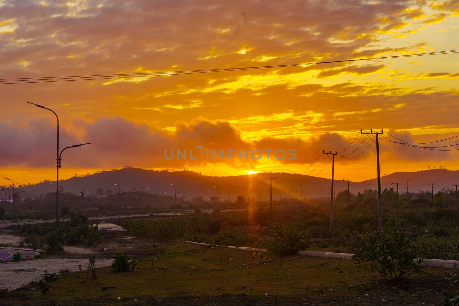 A breathtaking sunset paints the sky in vibrant hues of orange and pink, casting a warm glow over a vast landscape near Mandalika.