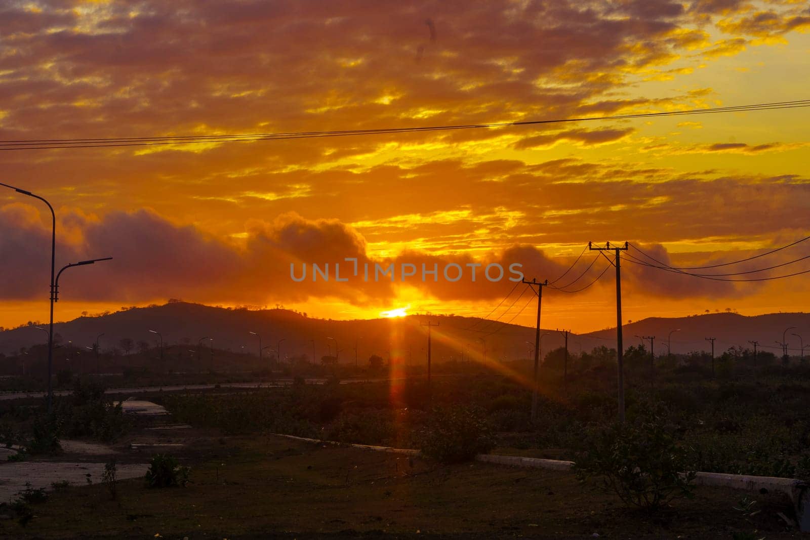 A breathtaking sunset paints the sky in vibrant hues of orange and pink, casting a warm glow over a vast landscape near Mandalika.