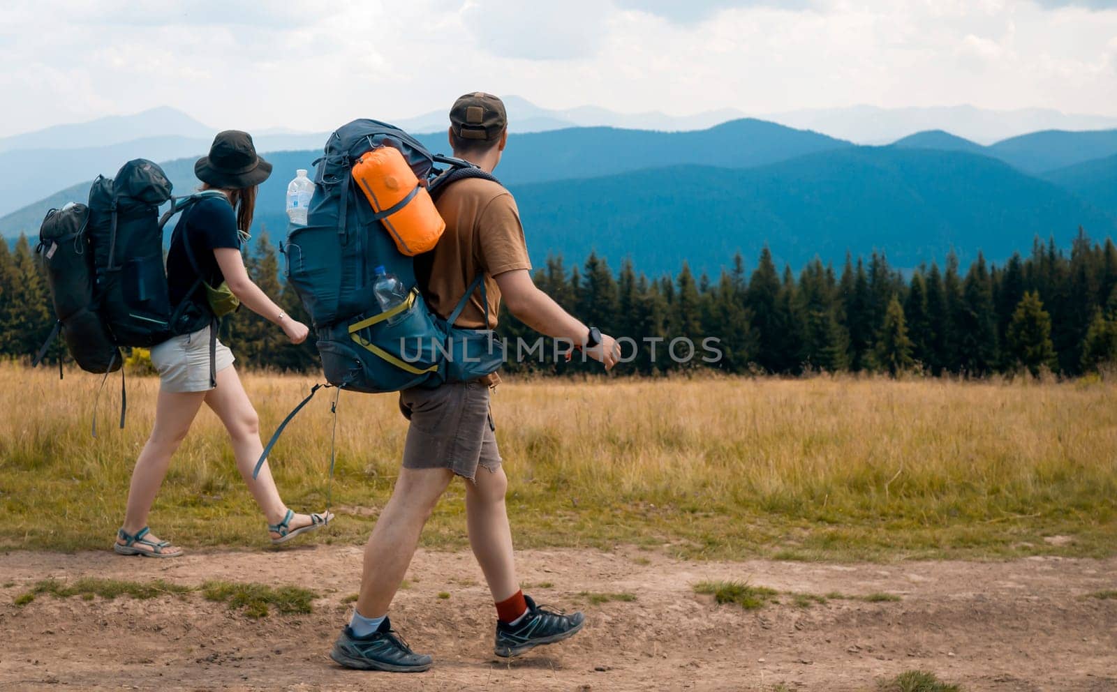 A young happy couple in love, a guy and a girl with a tourist backpack and equipment go on a trip, walk along trails, forest and mountains , friends actively spend time together in nature outdoor.