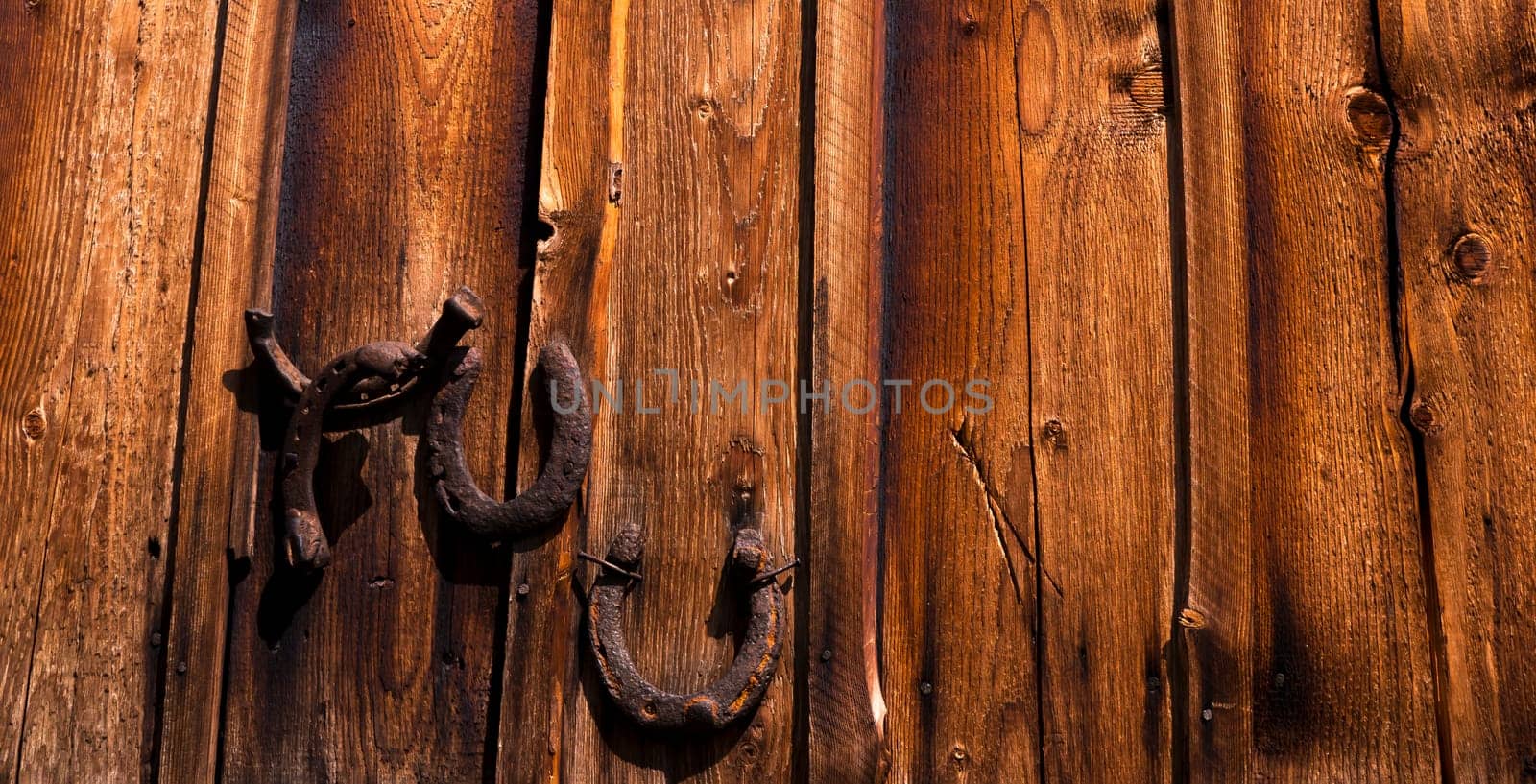 Background with old wooden boards with hanging horseshoes, vintage dark shade, textured and scratched, woody house wall or floor.