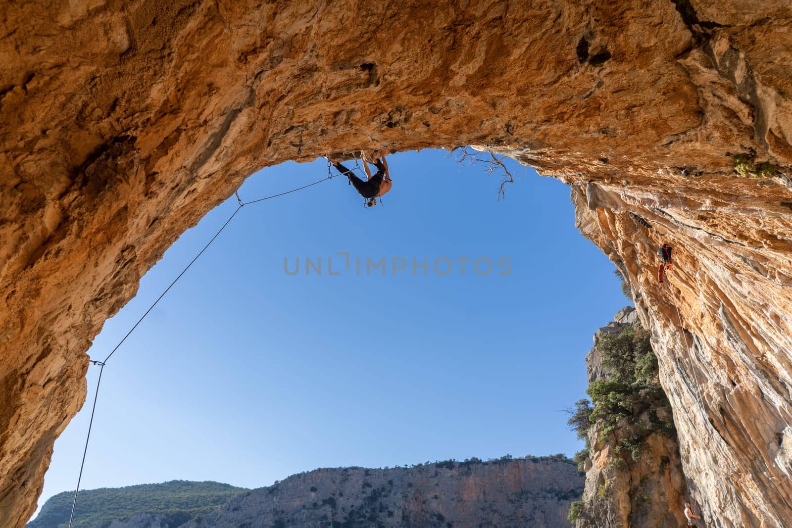 A man is professionally engaged in extreme sports, mountaineering and rock climbing, climbs the ceiling, the top of the cave against the blue sky on a sunny day in Twin Caves, Arcadia, Greece.