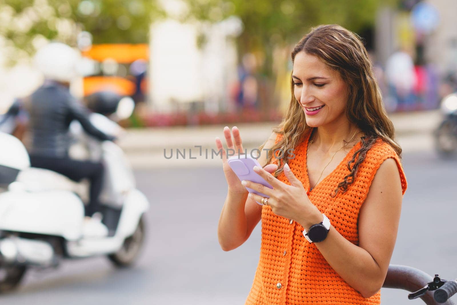 Latin woman scrolling the mobile in the street next to public rental bike service station