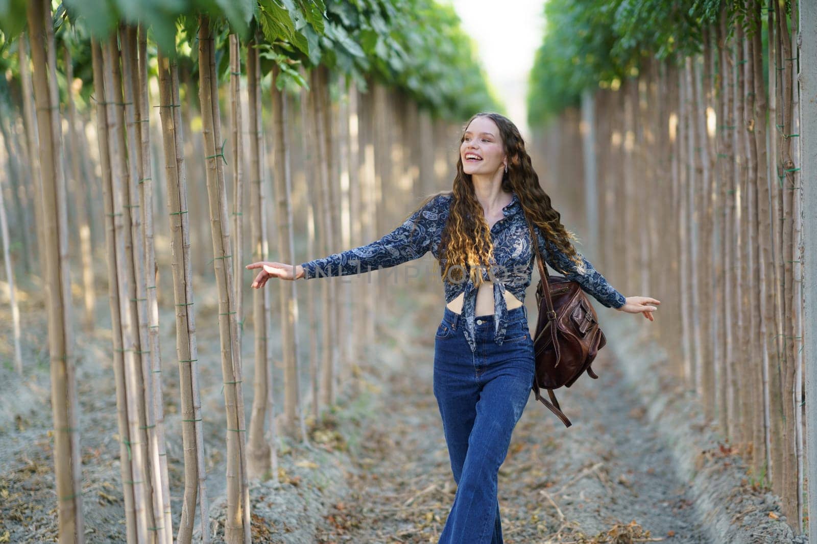 A joyful young woman with long hair strolls through a picturesque grove, savoring natures beauty and fresh air, radiating happiness and freedom, embracing the moment with delight