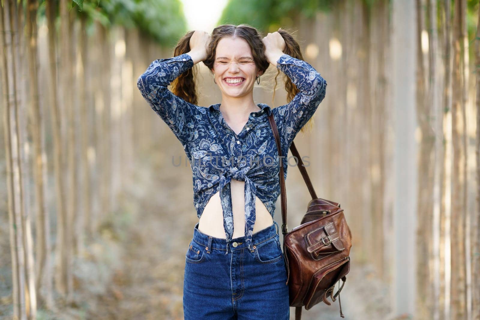 In a serene outdoor setting, surrounded by lush greenery, a joyful young woman in a colorful floral blouse playfully poses for the camera, radiating carefree happiness in that moment