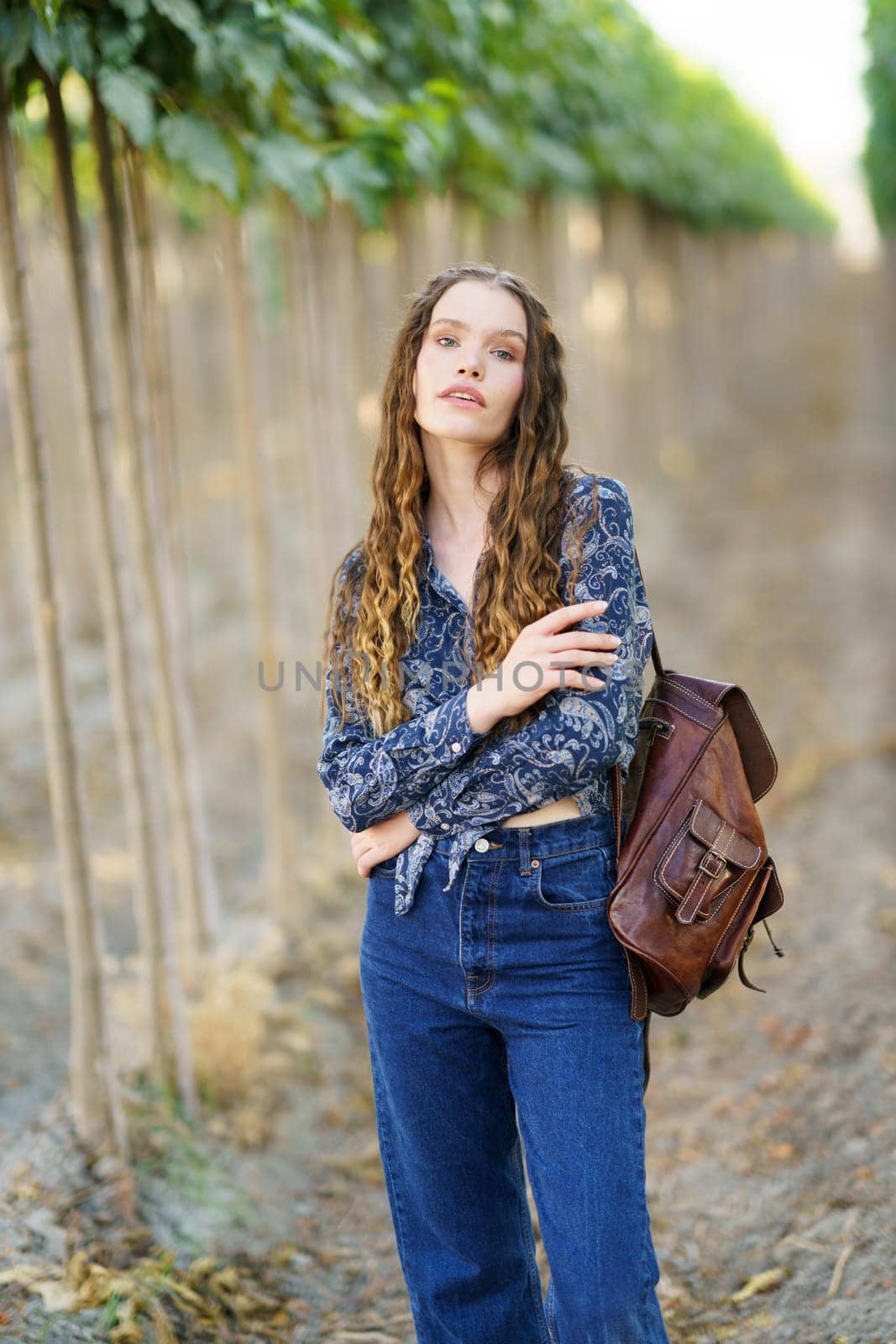 A stylish young woman poses in a beautiful vineyard, wearing a chic blouse and jeans, blending the natural beauty around her with her captivating style, enchanting all who see her