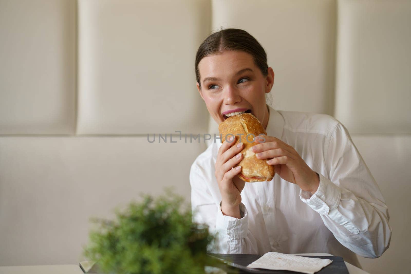 Cute elegant beauty businesswoman biting a sandwich sitting in a modern cafeteria