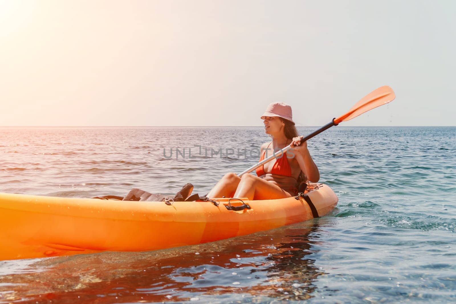 Happy smiling woman in kayak on ocean, paddling with wooden oar. Calm sea water and horizon in background