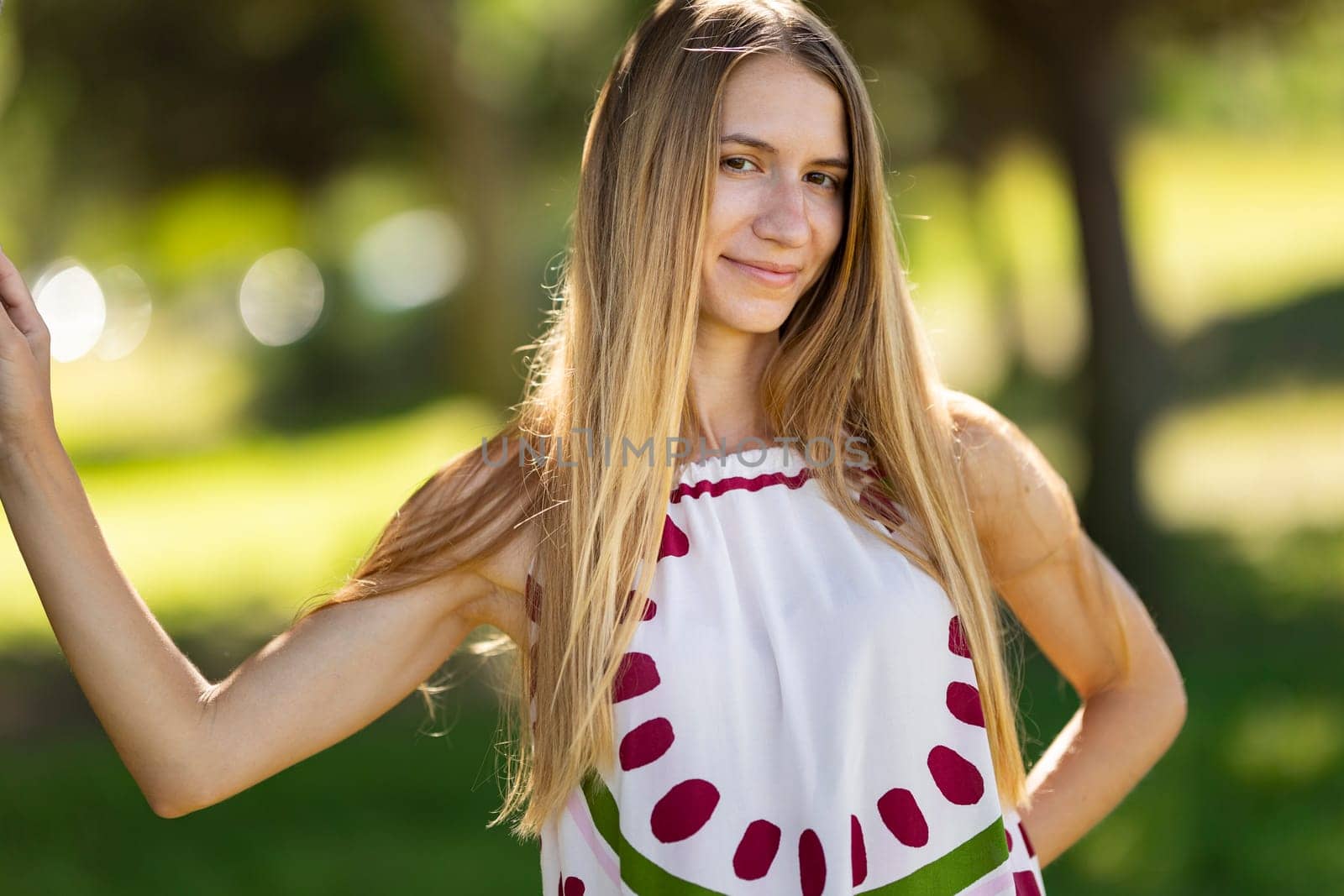 Beautiful blonde woman is posing in a park with her hand on her hip