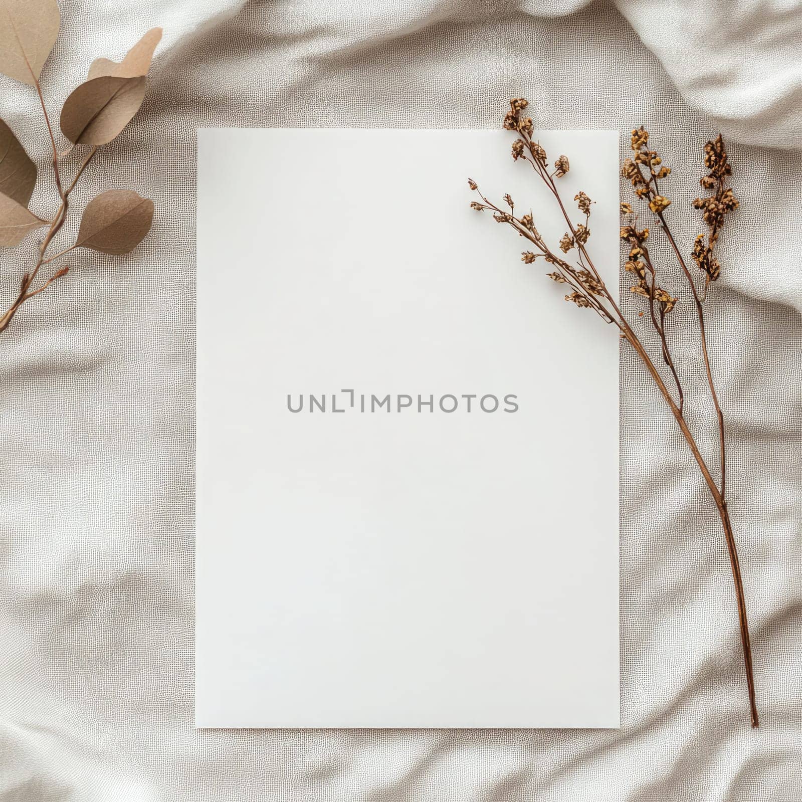 A piece of blank paper lies on a textured fabric backdrop surrounded by delicate dried flowers, creating an inviting space for writing or artistic projects.