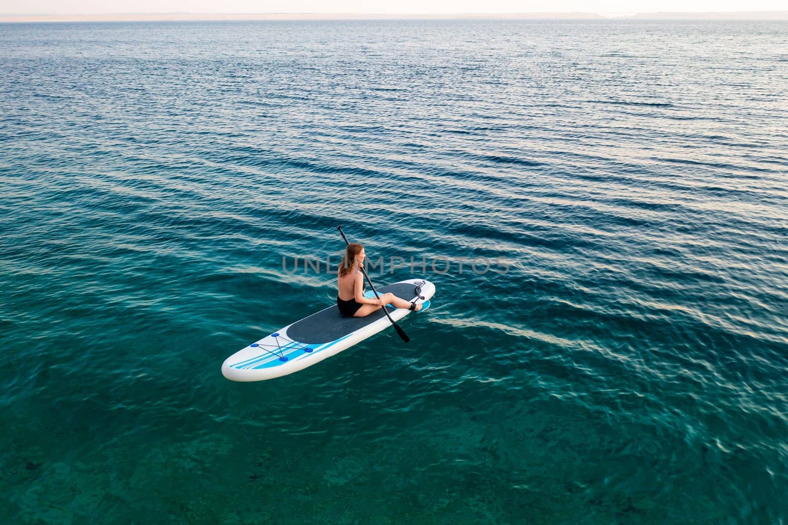 Woman paddle boarding on clear water during a calm twilight hour at the beach.