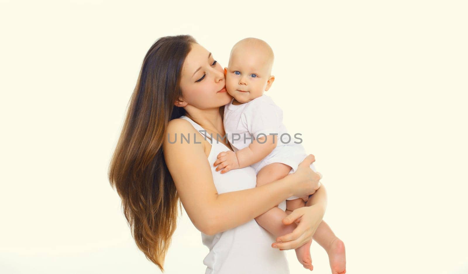 Portrait of happy mother kissing holding her baby, young mom and little child on white studio background
