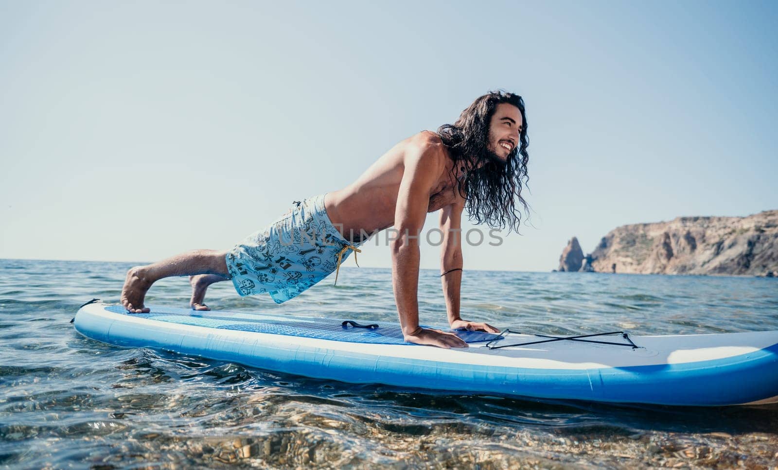 man sup yoga. Happy sporty man practising yoga pilates on paddle sup surfboard. male stretching doing workout on sea water. Modern individual male hipster outdoor summer sport activity
