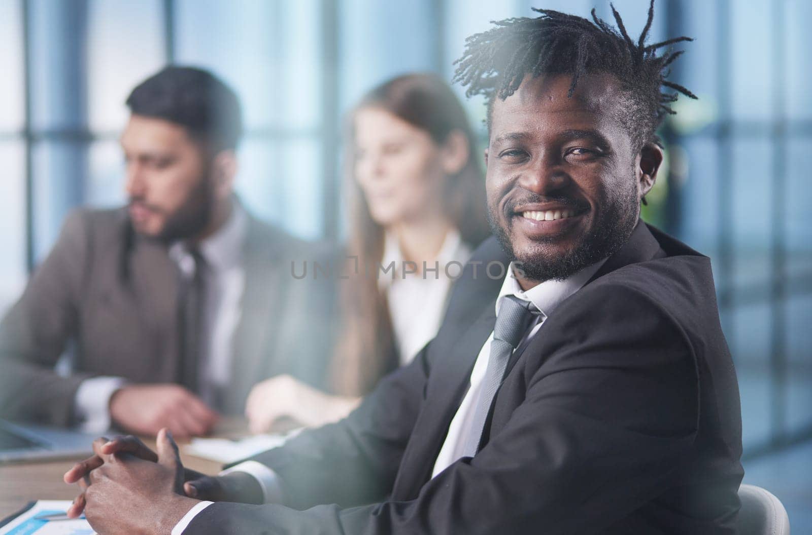 a black man posing at a table with his colleagues in the background