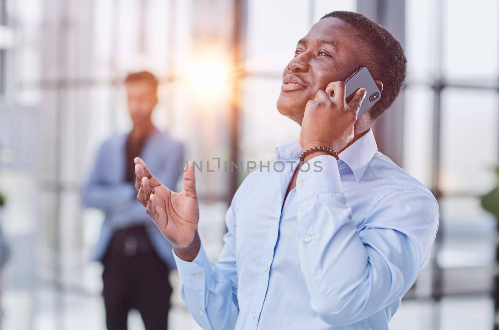 young Afro-American man walking through lobby of busy office building, talking on smartphon