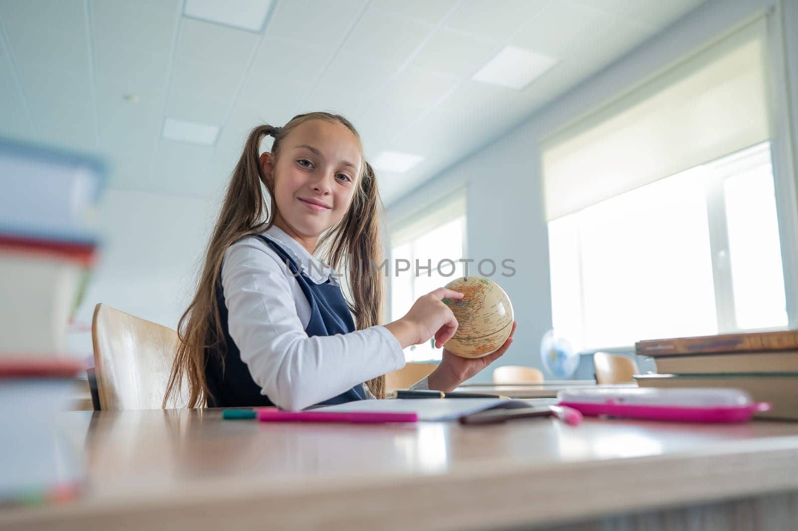 Caucasian schoolgirl sits at her desk at school and studies the globe. by mrwed54