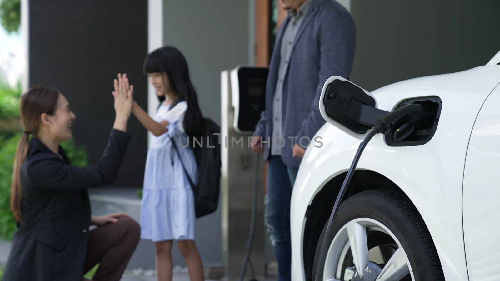 Progressive family with EV car and charging station prepare daughter to school. by biancoblue