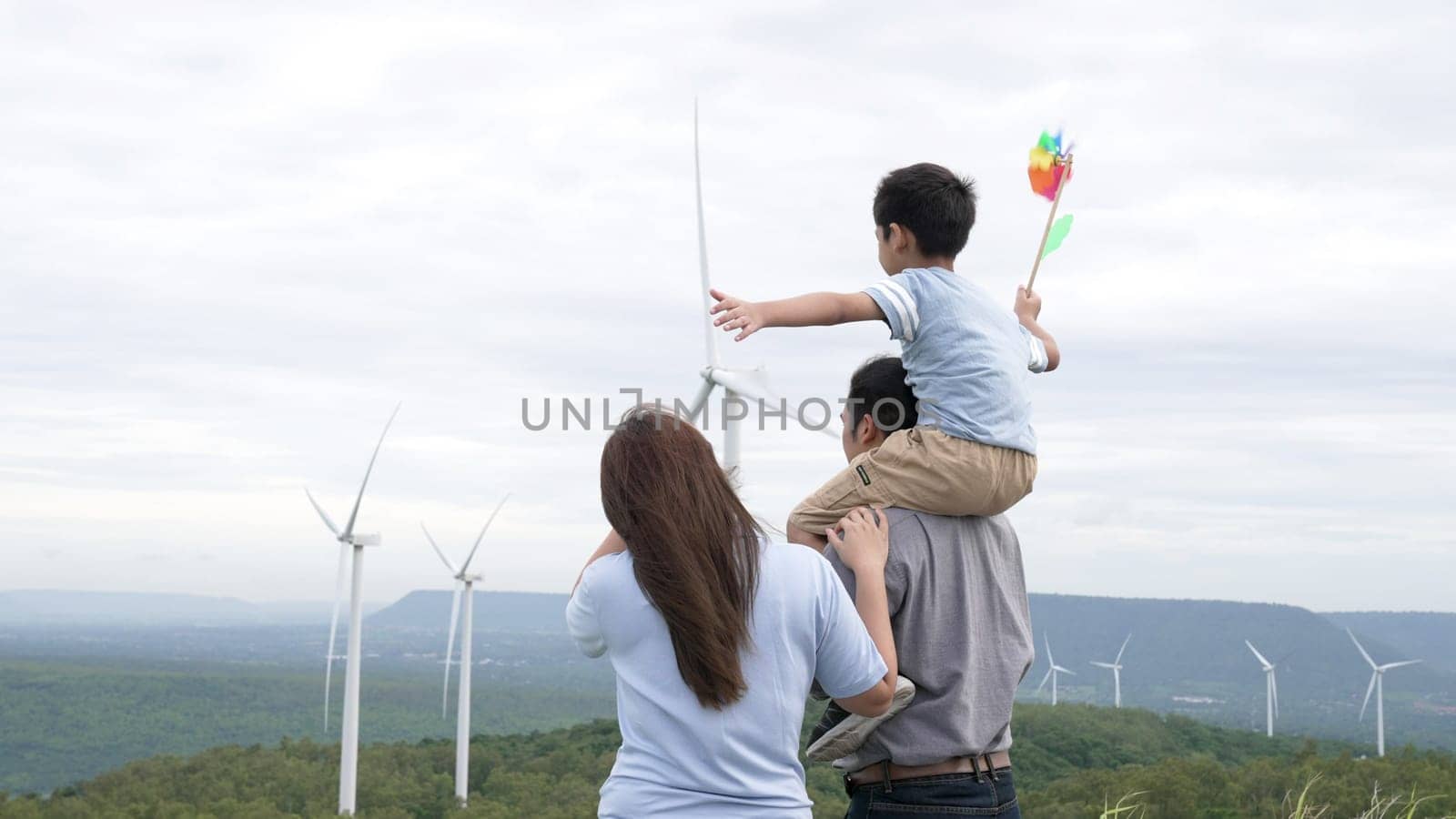 Concept of progressive happy family enjoying their time at the wind turbine farm. Electric generator from wind by wind turbine generator on the country side with hill and mountain on the horizon.