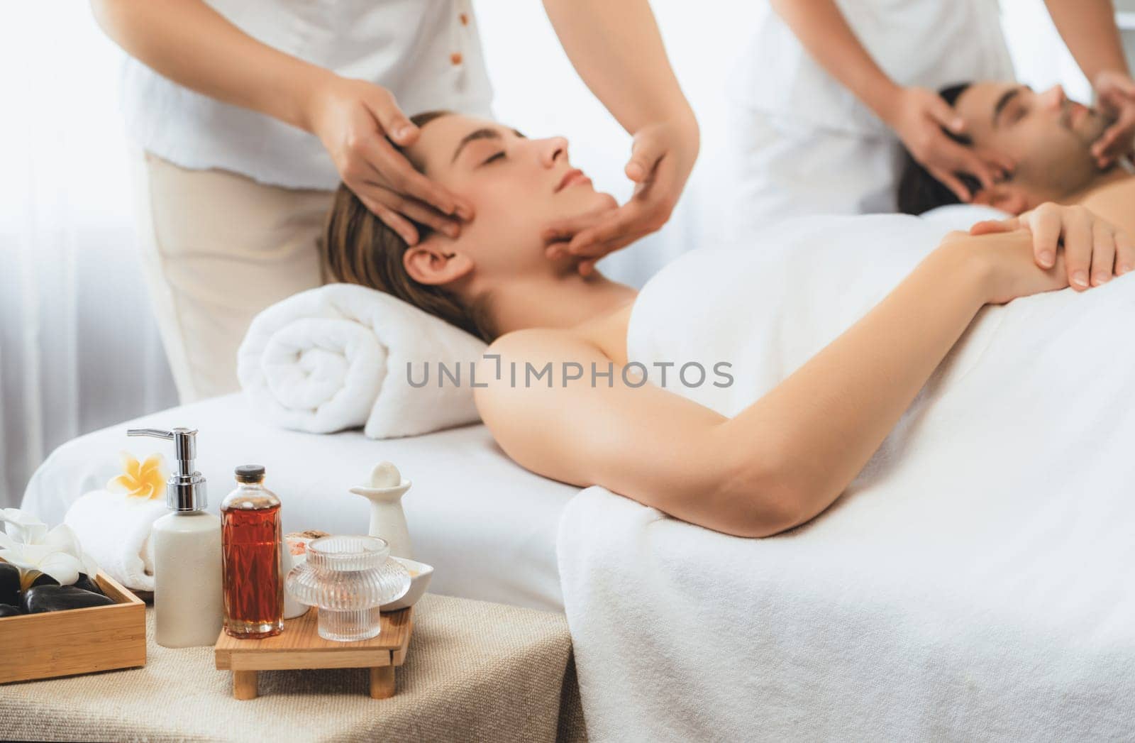 Caucasian couple enjoying relaxing anti-stress head massage and pampering facial beauty skin recreation leisure in dayspa modern light ambient at luxury resort or hotel spa salon. Quiescent