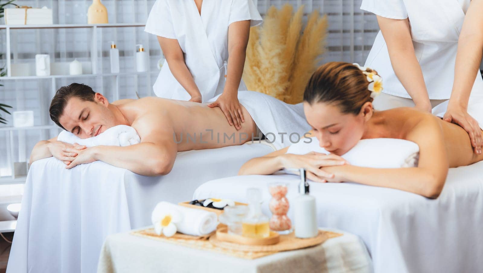 Caucasian couple customer enjoying relaxing anti-stress spa massage and pampering with beauty skin recreation leisure in day light ambient salon spa at luxury resort or hotel. Quiescent