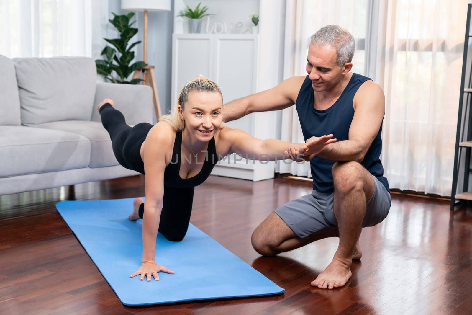 Happy active senior couple in sportswear being supportive and assist on yoga posture together at home. Healthy senior man and woman lifestyle with yoga exercise. Clout