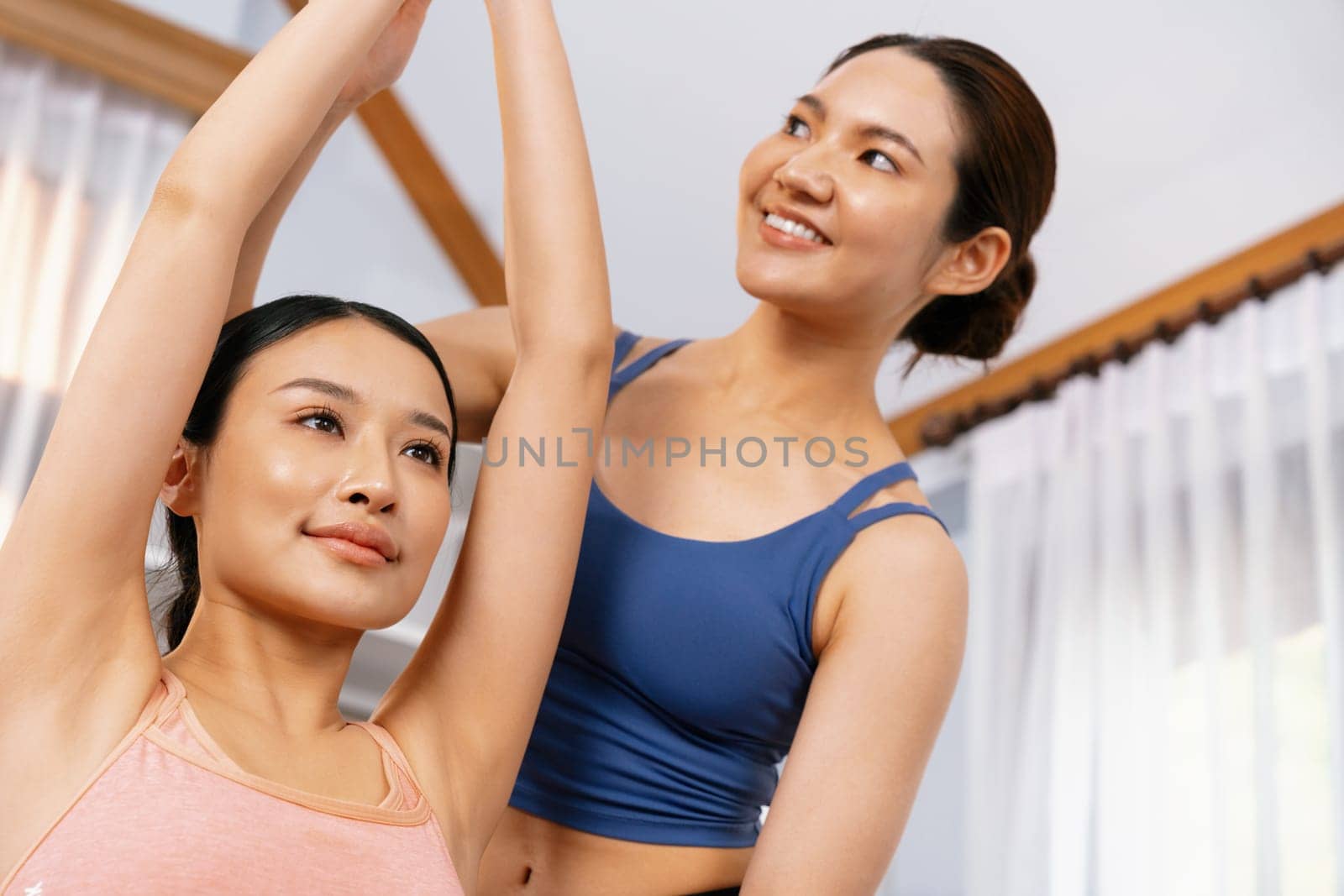 Asian woman in sportswear doing yoga exercise on fitness mat with trainer or workout buddy as home workout training routine. Healthy body care in yoga lifestyle people. Vigorous