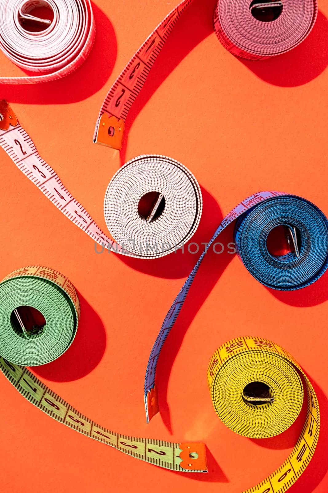 colorful measuring tapes top view on bright red background by Desperada