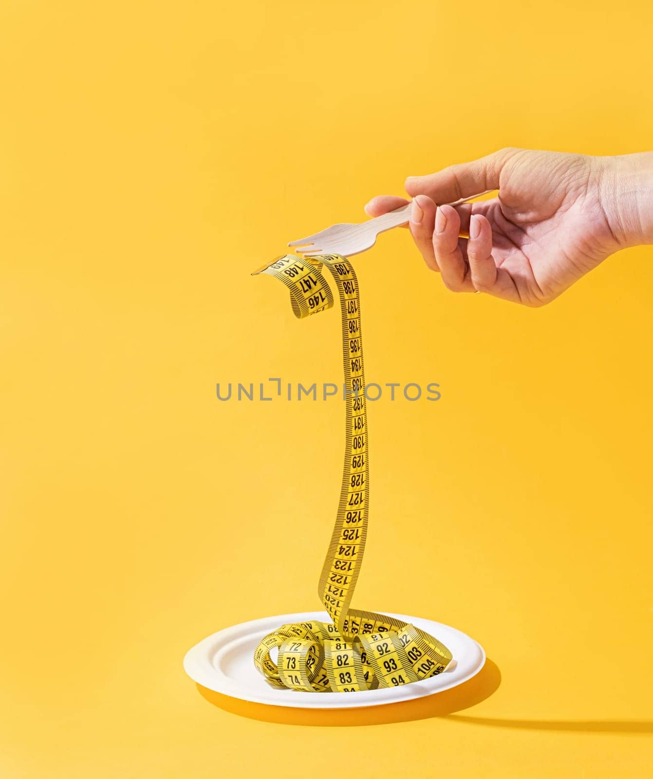 Dieting concept. woman hands holding colorful measuring tape front view on disposable plate on bright yellow background
