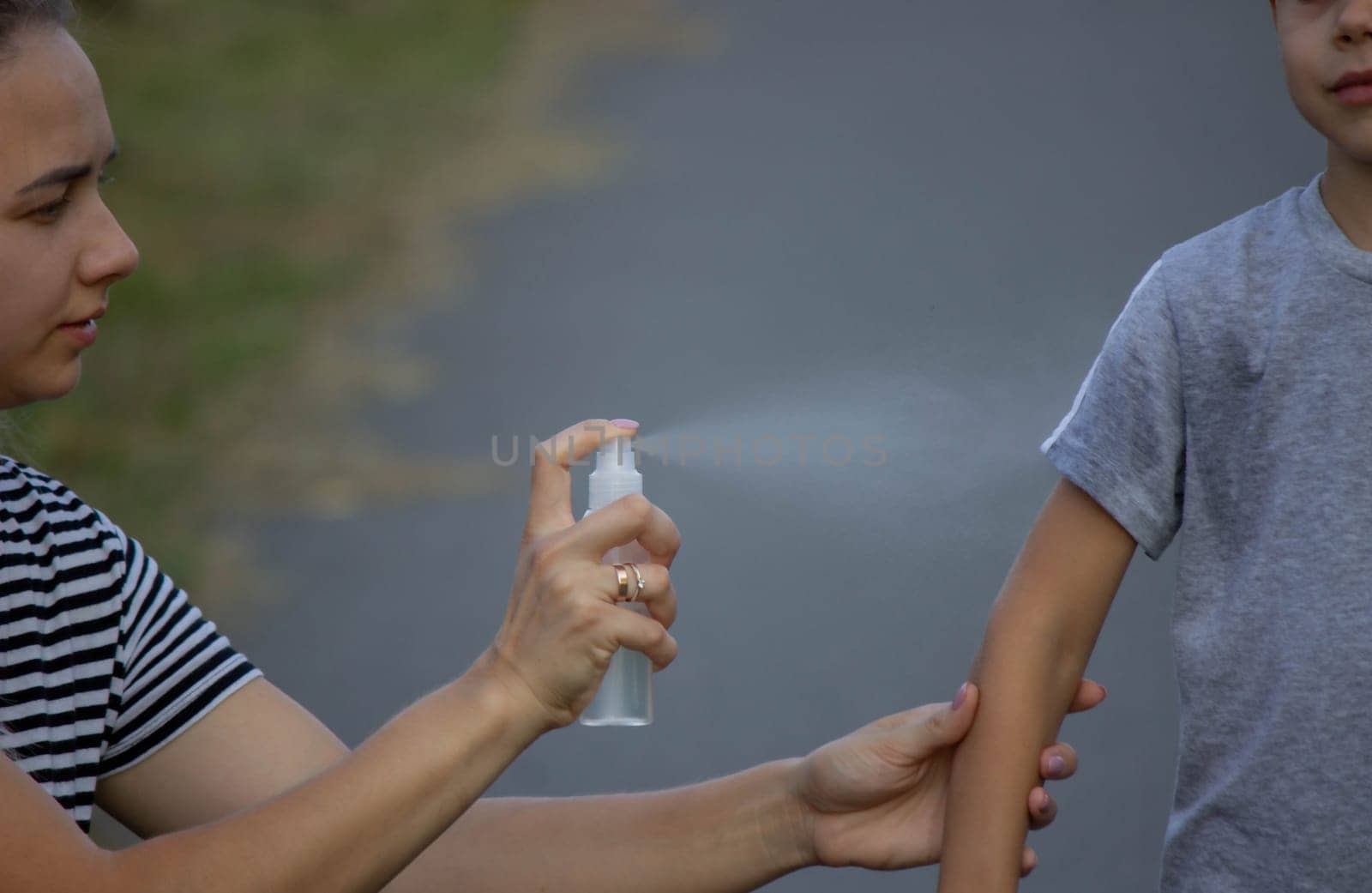 woman applies insect repellent to her son's hand in the park, close-up. Prevention of bites.
