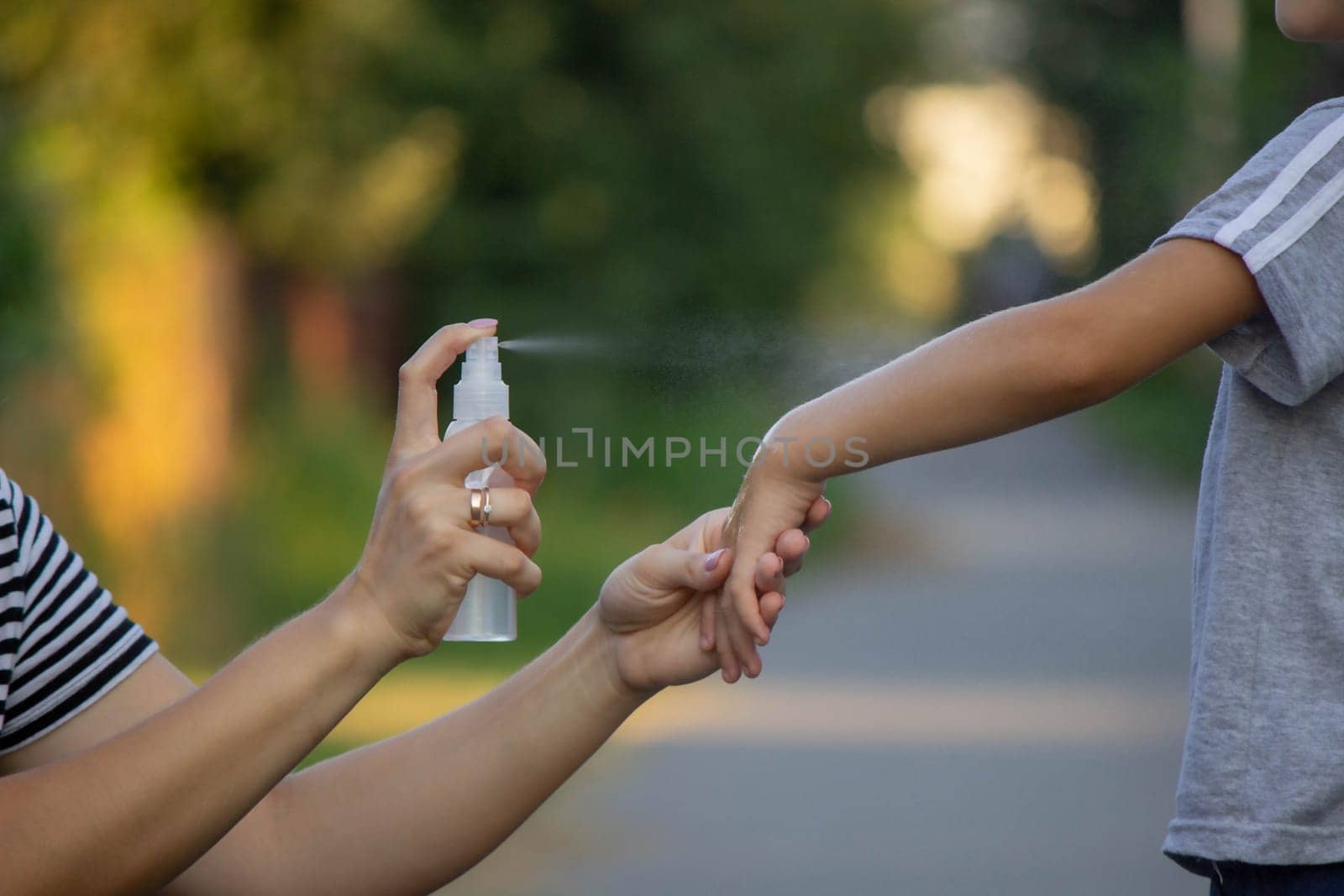 woman applies insect repellent to her son's hand in the park, close-up. Prevention of bites.