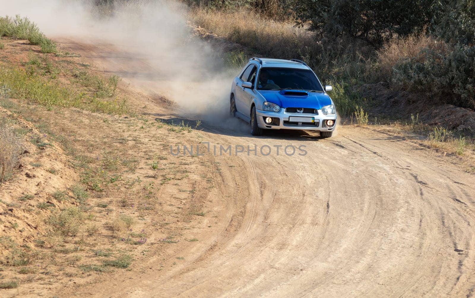 Sunny summer day. A sports hatchback takes a sharp turn on a dirt road and raises a cloud of dust