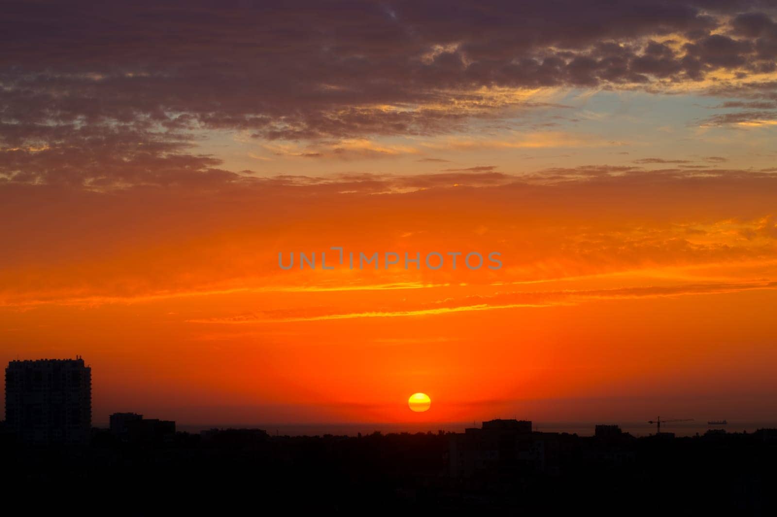 Dawn in the cloudy sky above the city. The sun barely appeared above the city roofs and colored the clouds