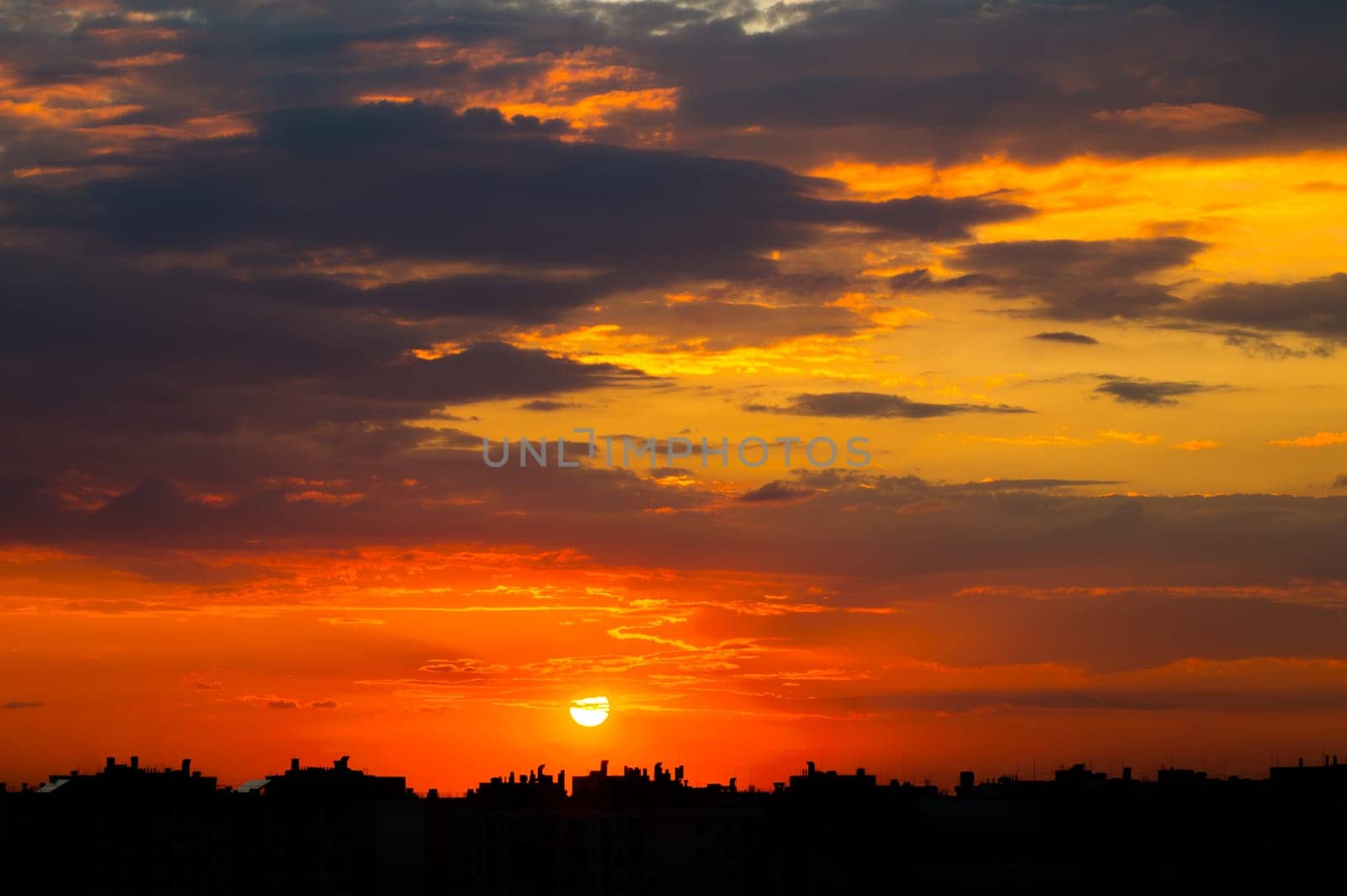 Cloudy sky over the roofs of the city. Sunset sun in the clouds above the silhouettes of buildings