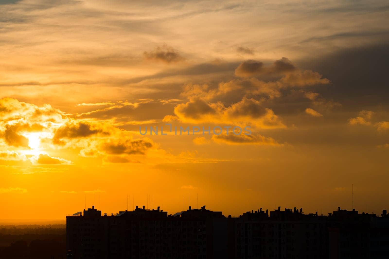 Whimsical clouds over the roofs of the city. The setting sun in the clouds above the silhouettes of buildings