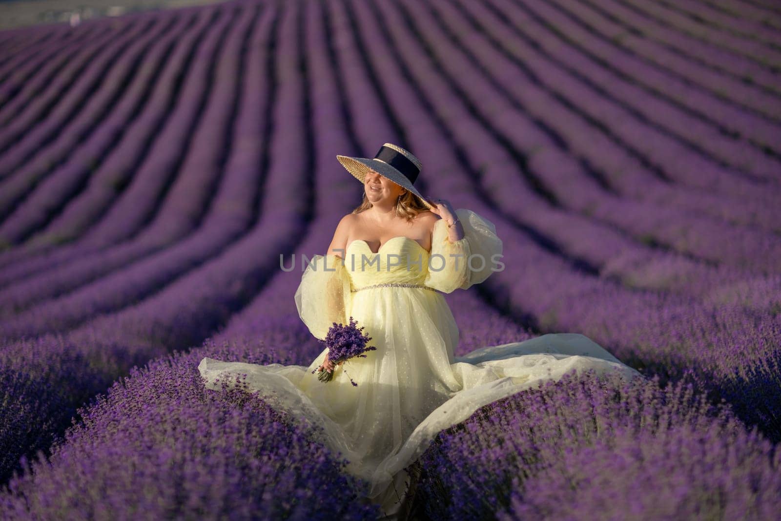 Woman poses in lavender field at sunset. Happy woman in yellow dress holds lavender bouquet. Aromatherapy concept, lavender oil, photo session in lavender.