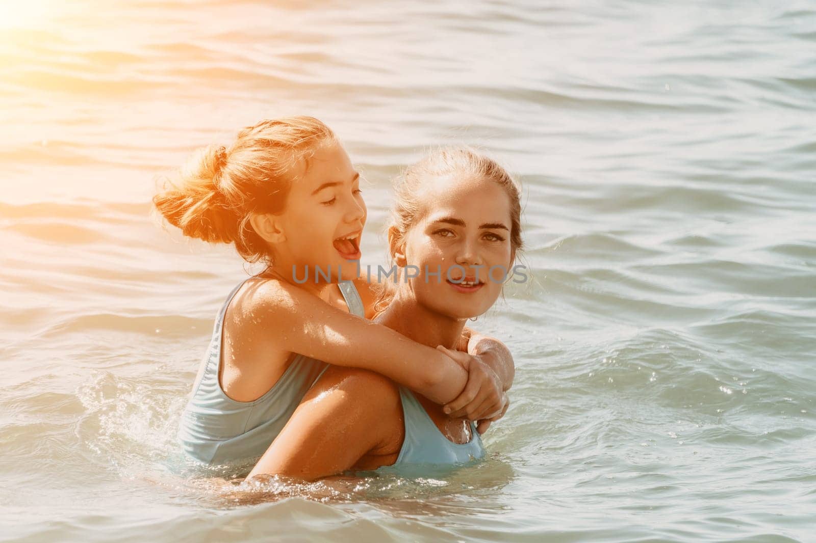 A young girl in blue swimsuit is having fun with her mom in the sea, they are laughing and splashing water, creating a joyful atmosphere.