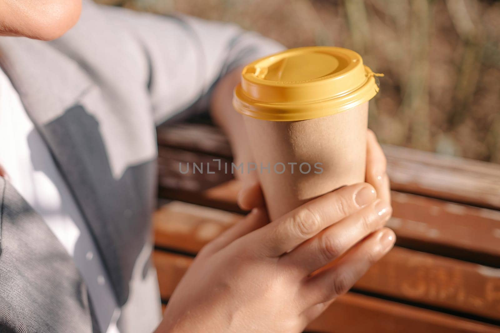 A person holding a coffee cup with a yellow lid. The person is wearing a gray jacket and white shirt