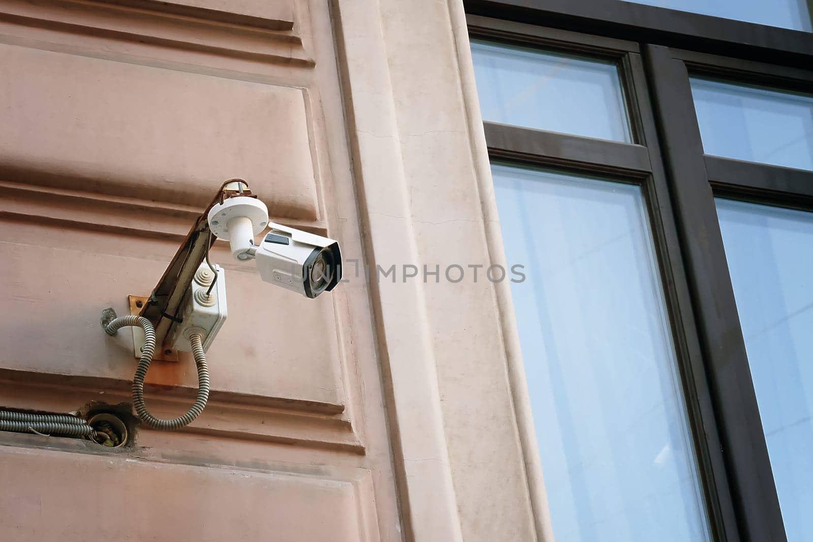 A contemporary surveillance camera is securely mounted next to the window on the exterior of a building, promoting safety and security to minimize robbery