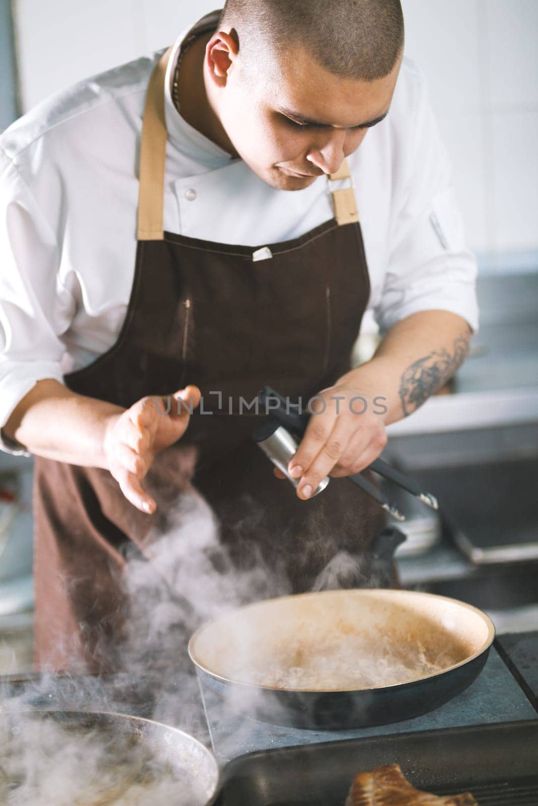 Young attractive male cook with uniform preparing a meat sause. The figure in a bent form.