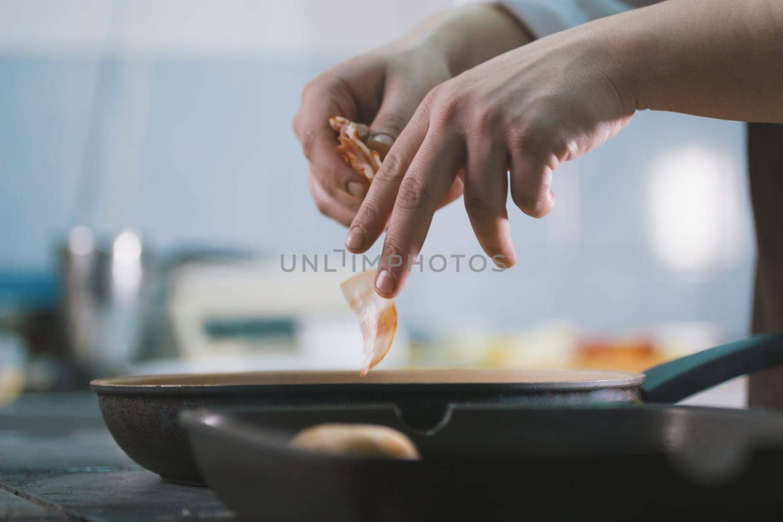 The chef fries bacon in a pan in the restaurant close up