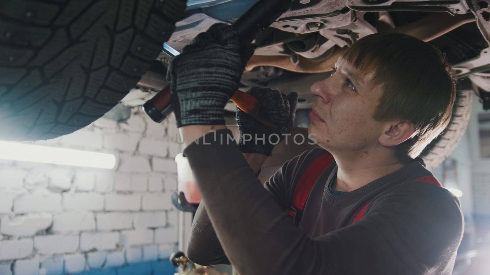 Mechanic with thr lamp is checking the bottom of car in garage automobile service, close up view