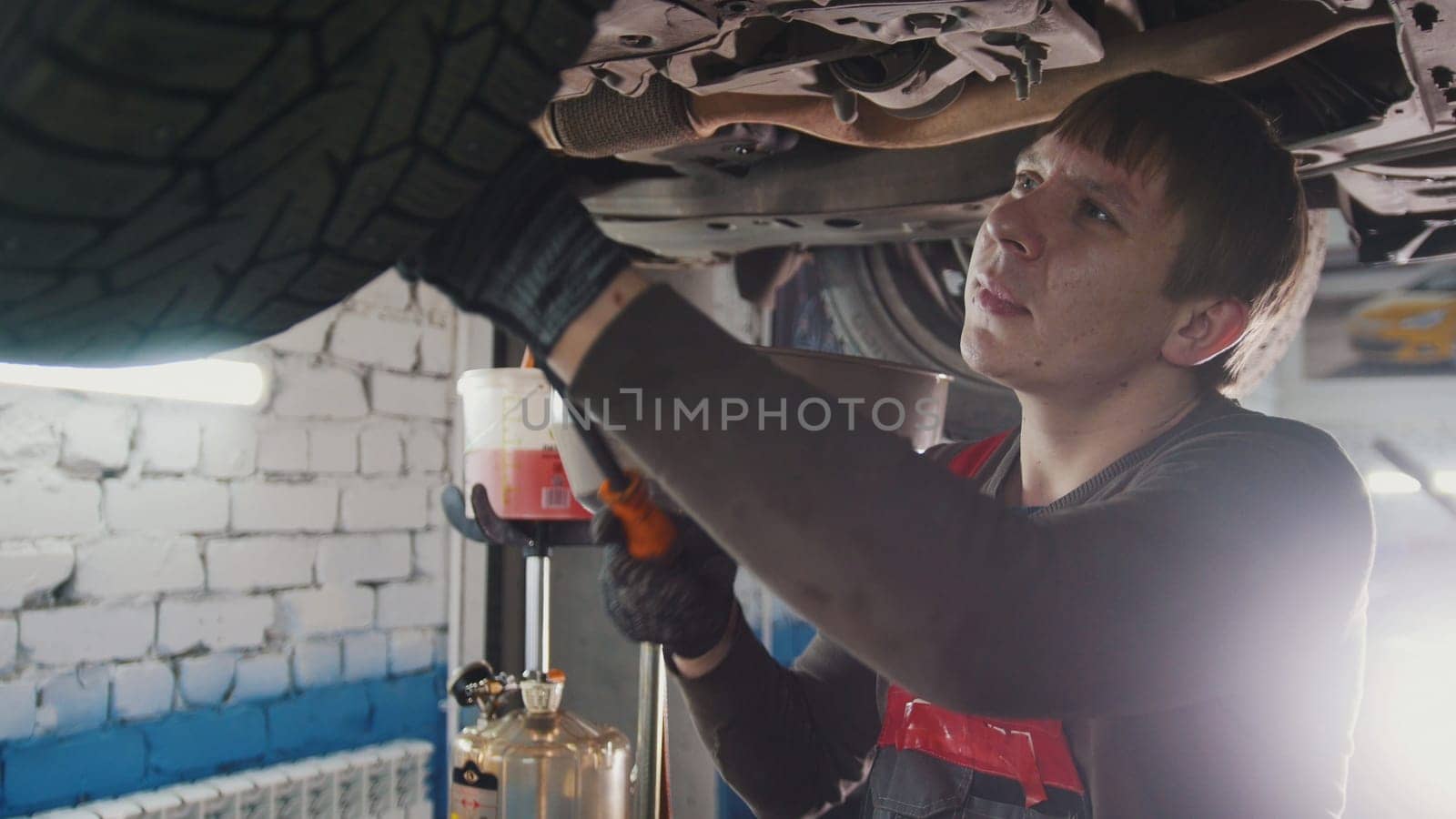 Mechanic with thr lamp is checking the bottom of car in garage automobile service, close up, telephoto