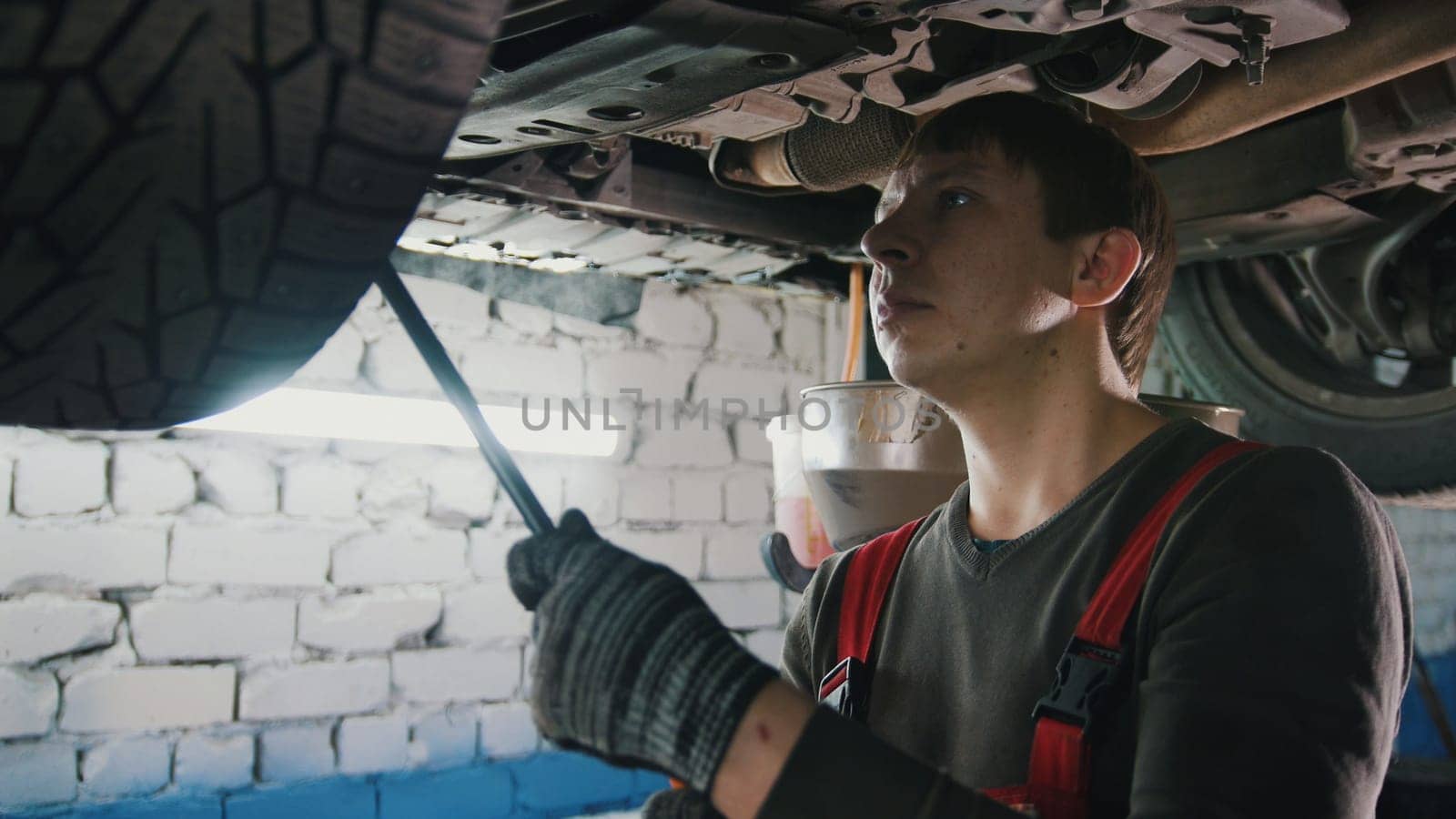 Mechanic with thr lamp is checking the bottom of car in garage automobile service, close up, telephoto