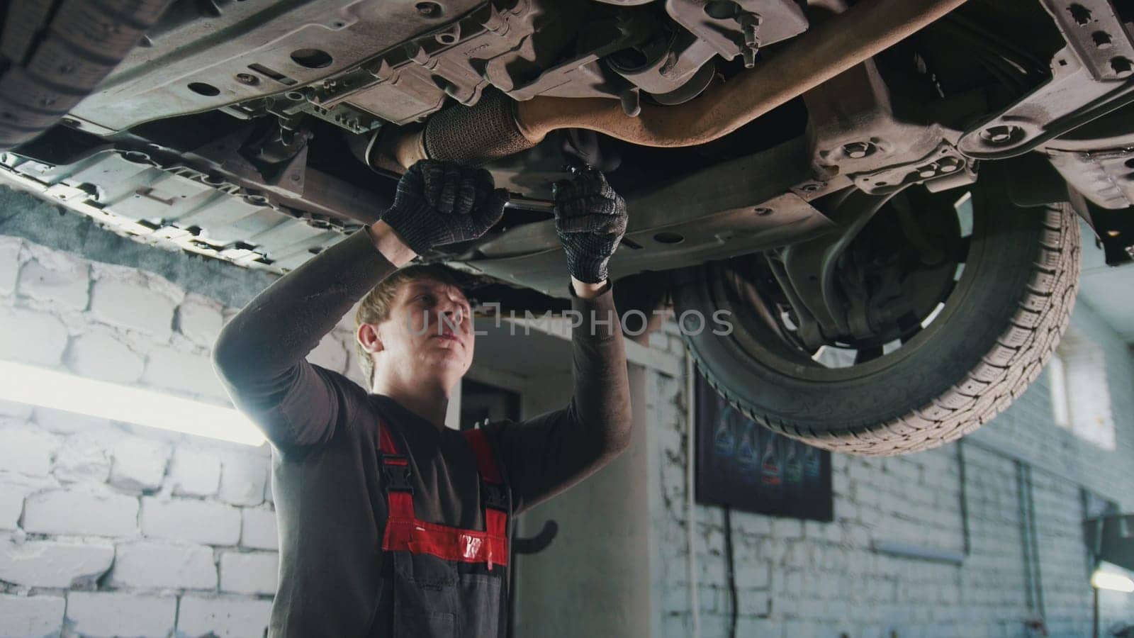 Mechanic with the wrench is repairing bottom of the car in garage automobile service, close up view