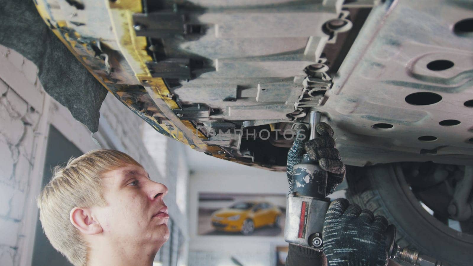 Car auto service - mechanic unscrews detail of car under bottom of vehicle, close up