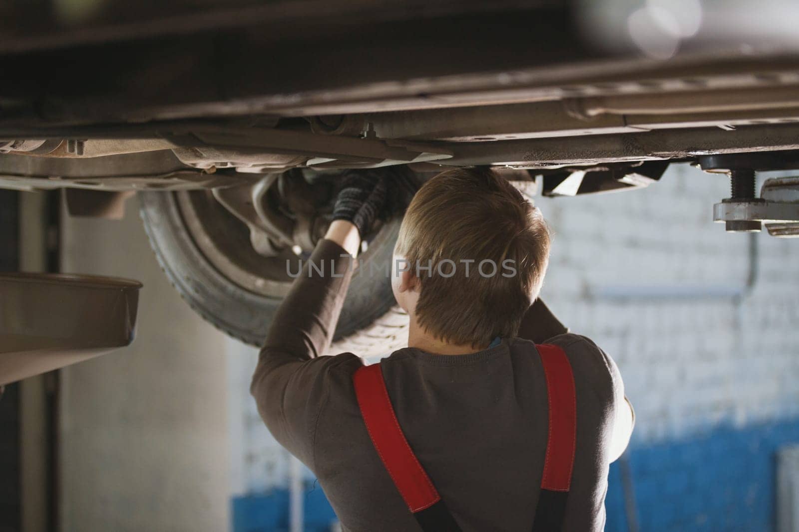 Mechanic unscrewing parts of automobile's bottom under lifted car, close up