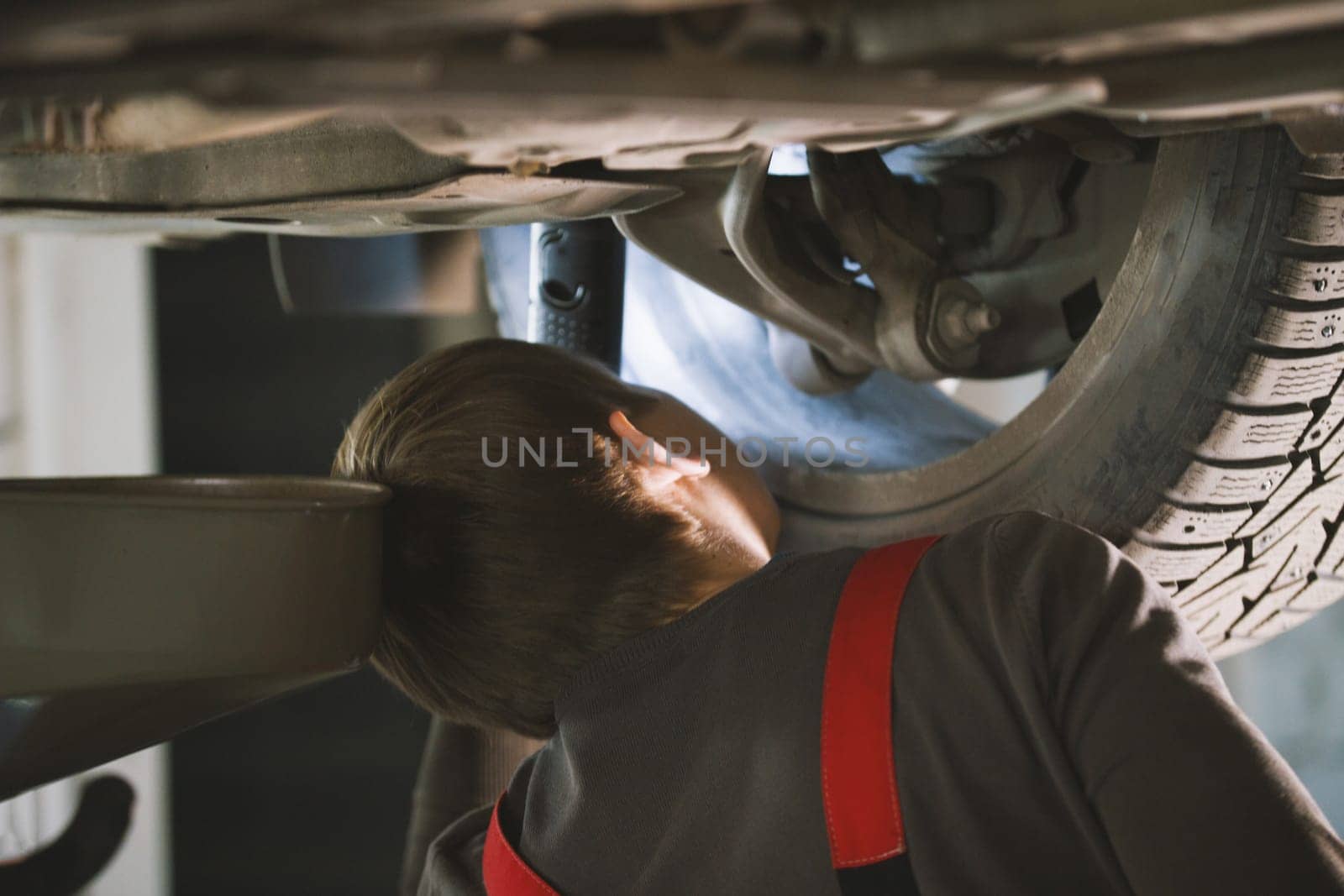 Mechanic unscrewing parts of automobile's bottom under lifted car, close up