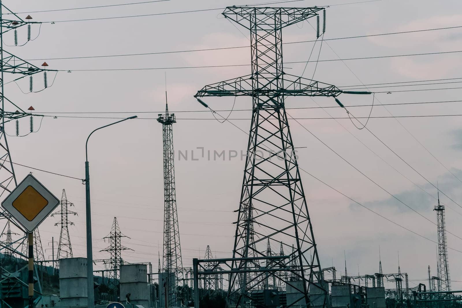 A low angle view of power lines and towers against a cloudy sky with a street lamp in the foreground.