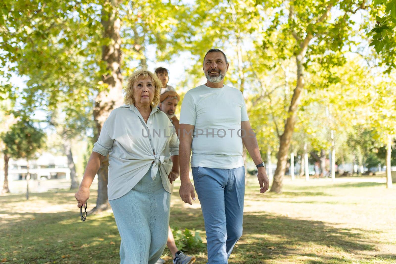 Family, spanning three generations, is enjoying a leisurely stroll through a sunny park
