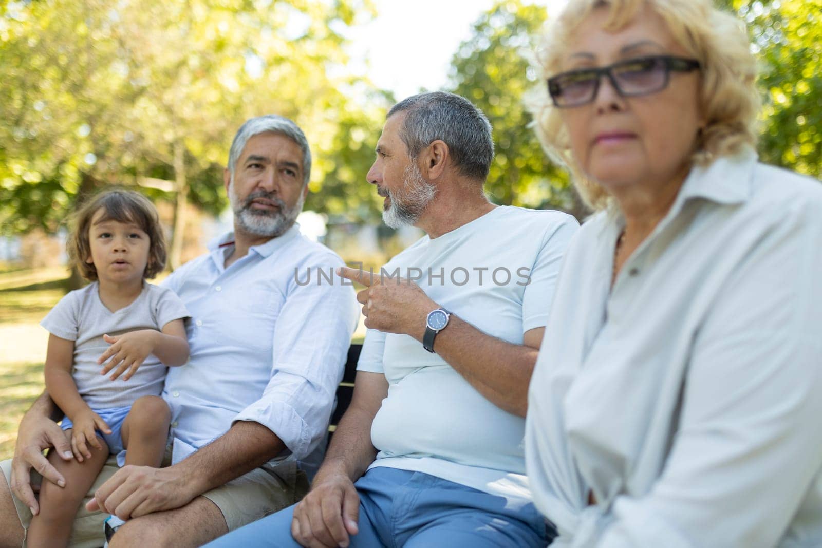 Senior woman is feeling excluded while her family is talking together on a park bench