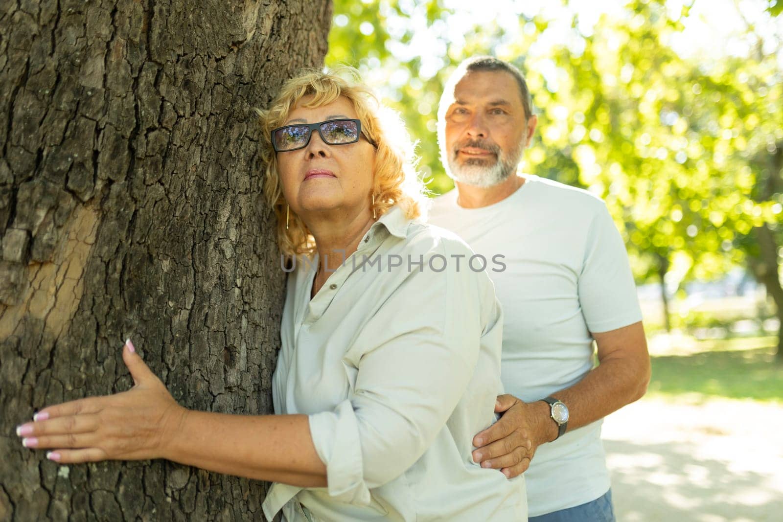 Retired couple holding each other and hugging a tree in the park on a sunny day